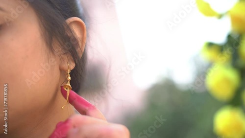Closeup shot of an Indian woman moving her golden earing with a blurred background. No face video.