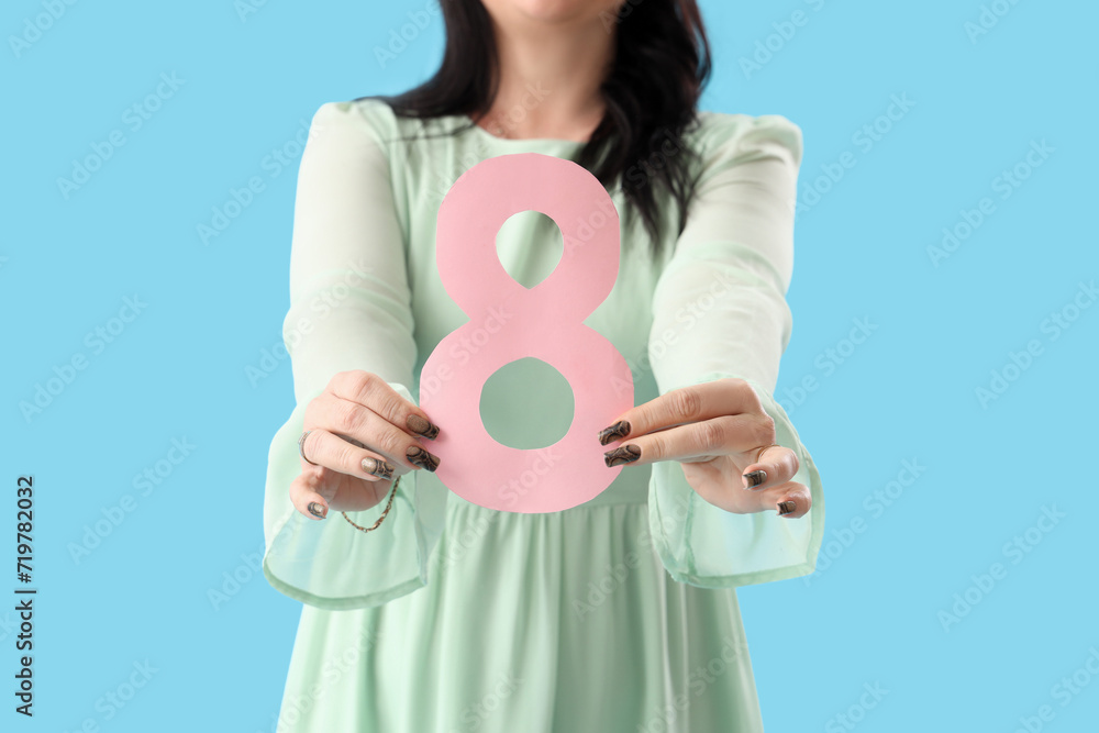 Beautiful mature woman with paper number 8 on blue background, closeup. International Women's Day Beautiful mature woman with paper number 8 on blue background, closeup. International Women's Day