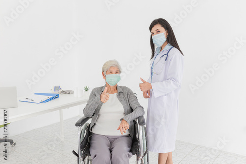 Asian doctor talk with old female patient about disease symptom, they show thumbs up sign with hand together, elderly health check up, they wear surgical mask