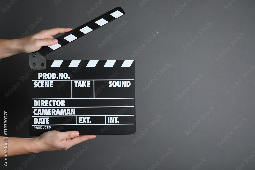 Woman holding clapperboard on dark grey background, closeup with space for text. Cinema production