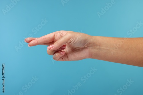 Woman crossing her fingers on light blue background, closeup