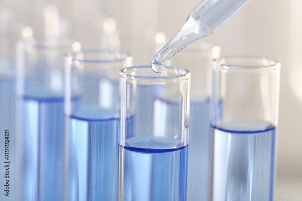 Laboratory analysis. Dripping light blue liquid from pipette into glass test tube on blurred background, closeup Laboratory analysis. Dripping light blue liquid from pipette into glass test tube on blurred background, closeup