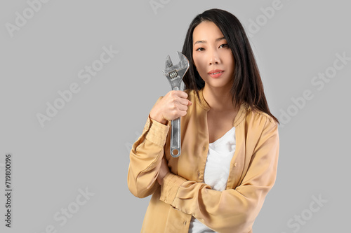 Young Asian woman with adjustable wrench on grey background. Women history month