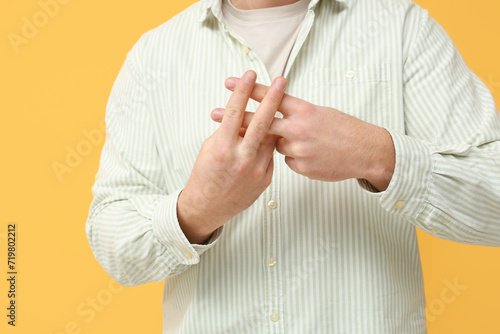 Man making hashtag sign with fingers on yellow background, closeup