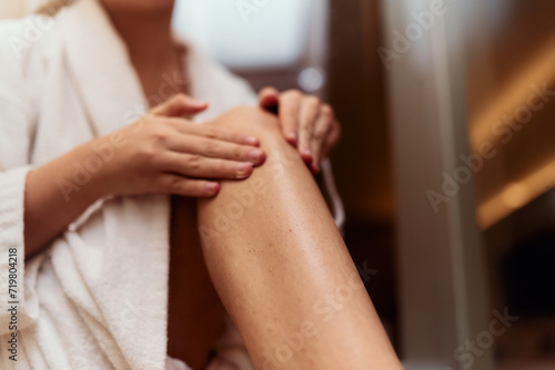 A woman indulges in her self care routine  pampering her skin after a relaxing bath by applying hydrating cream to her legs  embracing the essence of beauty and well being