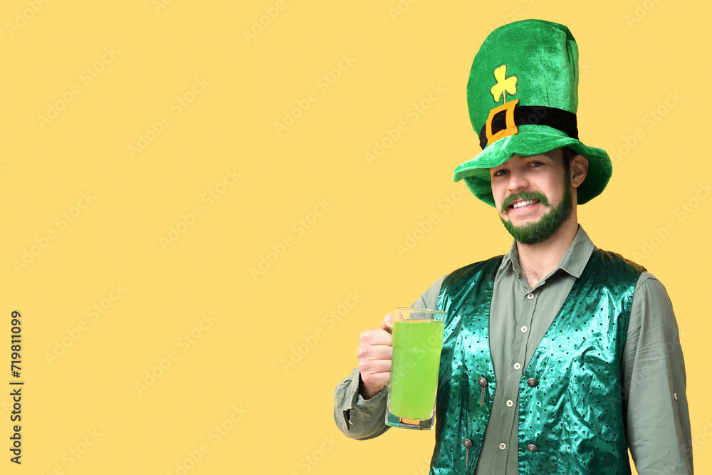 Fototapeta premium Happy young man in leprechaun hat with green beard holding glass of beer on yellow background. St. Patrick's Day celebration
