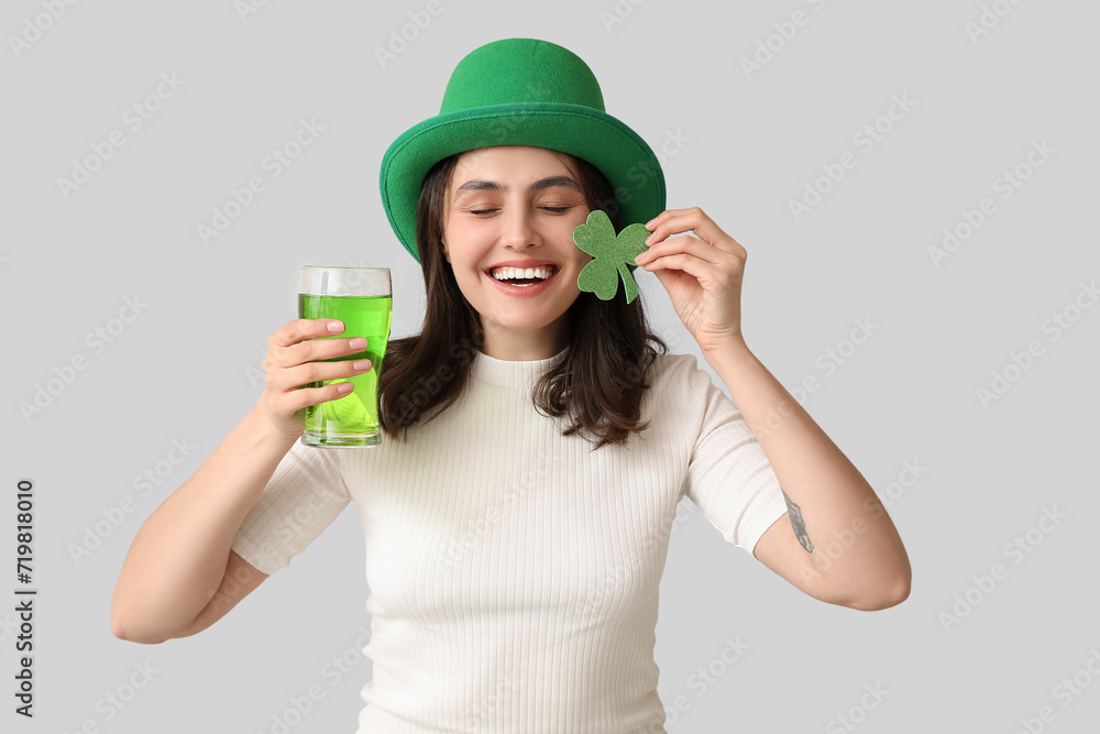 Beautiful young woman in leprechaun hat with glass of beer and clover on grey background. St. Patrick's Day celebration Beautiful young woman in leprechaun hat with glass of beer and clover on grey background. St. Patrick's Day celebration