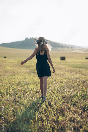 a girl with blond hair and a wreath of flowers on her head walks through the fields in summer
