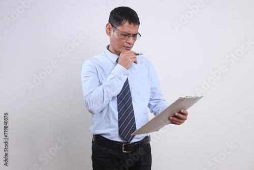 Adult Asian businessman looking and analyzing document at clipboard with serious expression