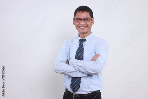 Portrait of happy adult Asian businessman with formal clothes and looking at camera while standing in crossed arms