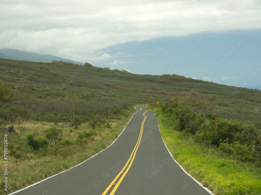 Driving by lonely Maui road with hills and green field on roadside on sunny day, Hawaii Driving by lonely Maui road with hills and green field on roadside on sunny day, Hawaii
