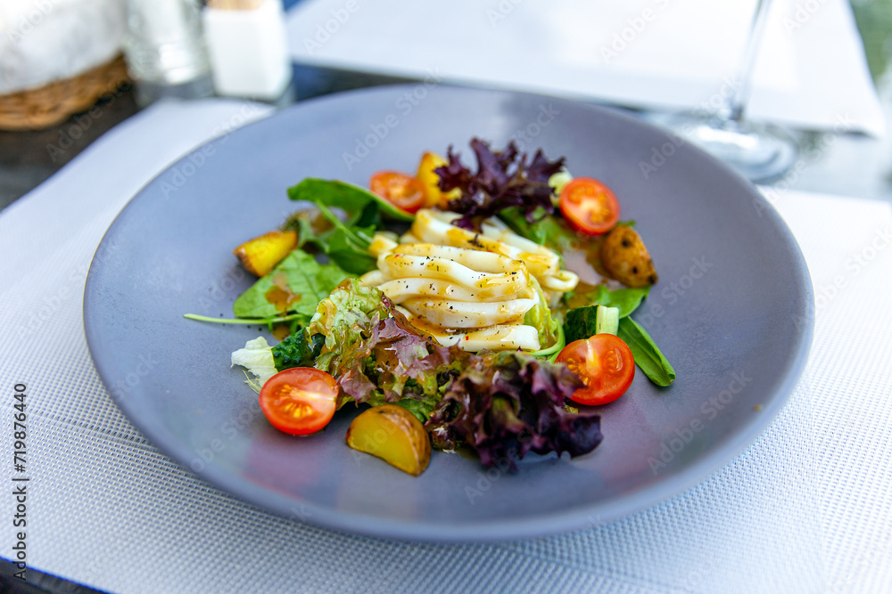 Delicious salad with squid, boiled potatoes and fresh vegetables, served with olive oil Delicious salad with squid, boiled potatoes and fresh vegetables, served with olive oil