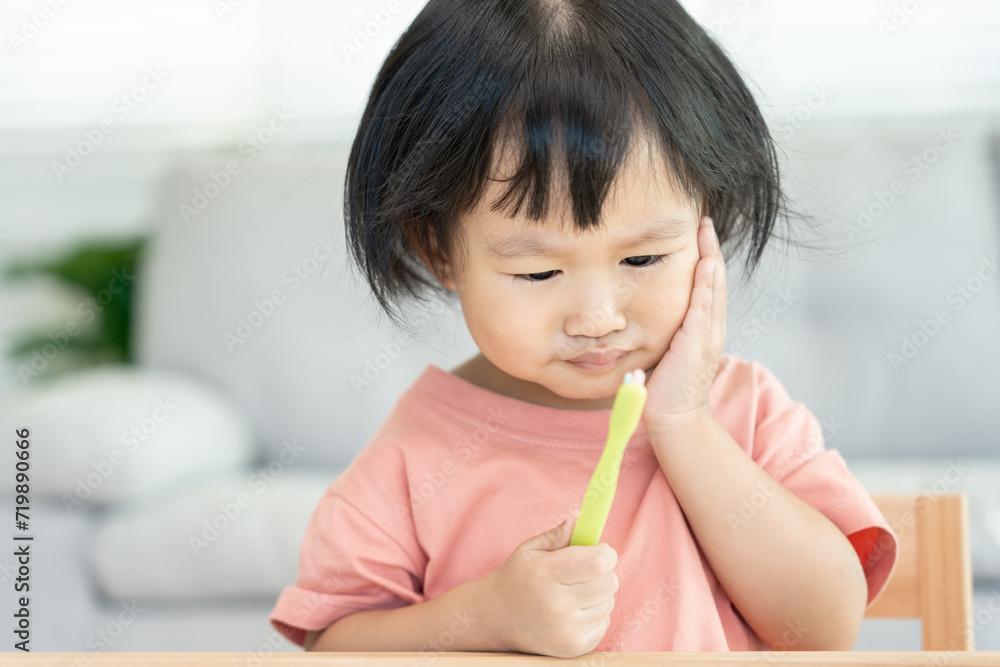 little asian girl presses hand to cheek, suffers from pain in tooth. Teeth decay, dental problems, child emotions and facial expression, oral health care, reducing sweets, fluorine coating little asian girl presses hand to cheek, suffers from pain in tooth. Teeth decay, dental problems, child emotions and facial expression, oral health care, reducing sweets, fluorine coating