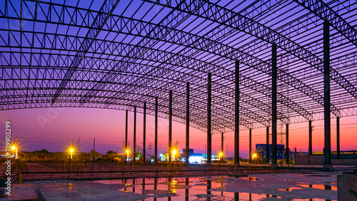 Silhouette curve metal roof beam with columns of large factory building outline structure in construction site at industrial settlement zone against twilight sky background