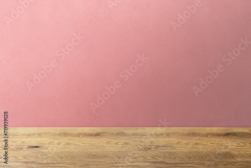 木目のあるナチュラルな木のテーブルと凹凸のあるピンクの壁の背景
