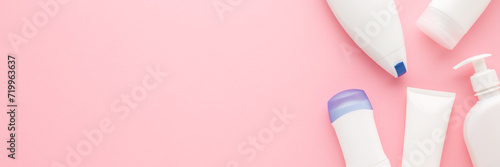 Different white plastic cosmetic bottles on light pink table background. Pastel color. Care about clean and soft body skin. Beauty product. Closeup. Wide banner. Empty place for text. Top down view. photo