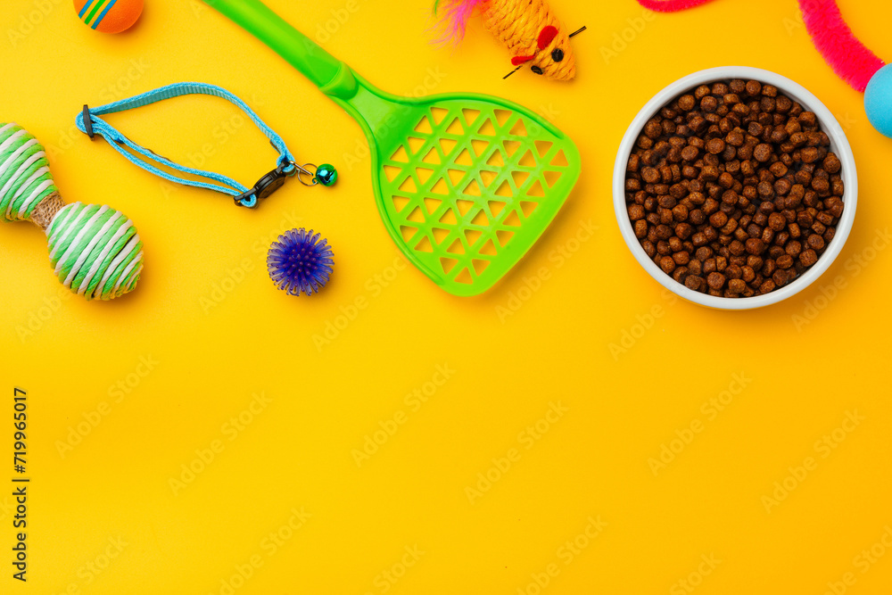 Cat bowl with dry food and toys on yellow background studio shot Cat bowl with dry food and toys on yellow background studio shot