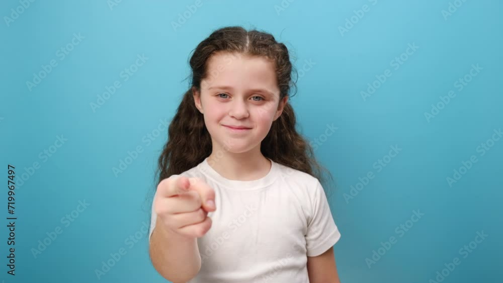 Portrait of pretty little girl child looking pointing finger at camera with smile, choosing you, expressing positive, wearing white t-shirt, posing isolated over blue color background wall in studio Portrait of pretty little girl child looking pointing finger at camera with smile, choosing you, expressing positive, wearing white t-shirt, posing isolated over blue color background wall in studio
