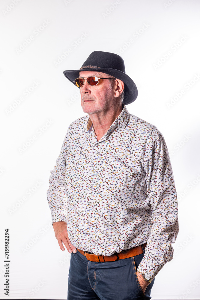 This image presents a senior man looking off into the distance, wearing a casual patterned shirt and a stylish fedora hat paired with sunglasses. The relaxed fit of his shirt and the comfortable This image presents a senior man looking off into the distance, wearing a casual patterned shirt and a stylish fedora hat paired with sunglasses. The relaxed fit of his shirt and the comfortable