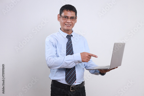 Cheerful adult Asian businessman wear glasses, shirt and tie pointing at laptop with happy expression