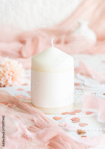 Candle with blank label near pink decorations, hearts and tulle on white table close up, mockup