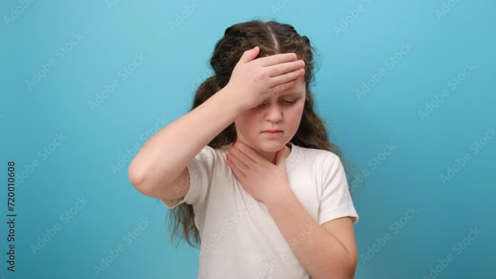 Portrait of unhealthy sick little girl child having flu symptoms, coughing, keeping hand near mouth, wearing white casual t-shirt, posing isolated over plain blue color background wall in studio Portrait of unhealthy sick little girl child having flu symptoms, coughing, keeping hand near mouth, wearing white casual t-shirt, posing isolated over plain blue color background wall in studio