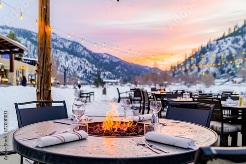 Fototapeta Naklejka Na Ścianę i Meble -  A romantic outdoor dining setup with a fire pit at a snowy mountain resort during a beautiful sunset.