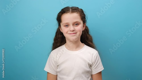 Portrait of cute little girl wearing white T-shirt holding palm over her eyes, looking into distance with attentive view, watching horizon, far future, posing isolated on blue studio background wall