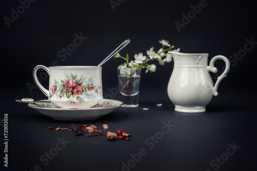 Still life with a beautiful fine china tea cup and tea accessories on a black background