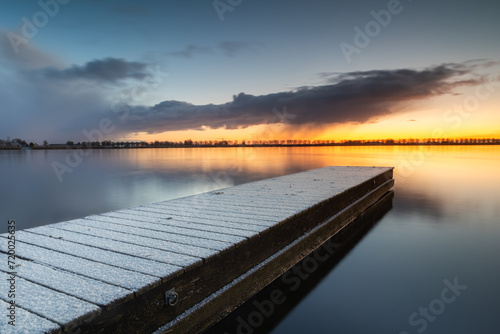 Snow-covered jetty in Lake Dirkshorn during sunrise. The layer of snow that fell during the cold night has settled on the jetty.