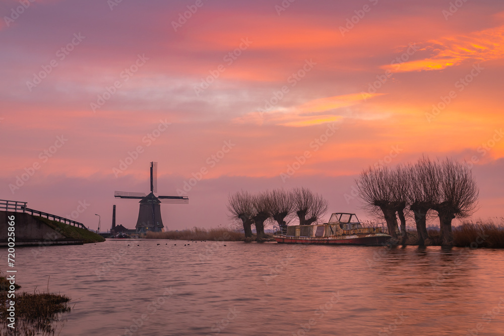 The Kaagmolen, pollard willows, and a boat in Spanbroek (North Holland) under a brightly colored sky. The Kaagmolen is a polder mill built in 1654 for draining the Kaagpolder. 