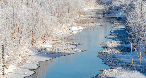 The river flows in winter along frozen snow-covered banks.