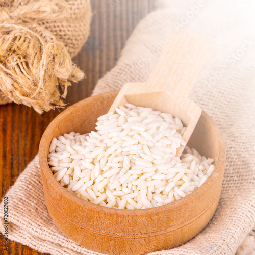 White uncooked Thailand jasmine rice in small burlap bag with wooden spoon on wood tablle on sunlight photo