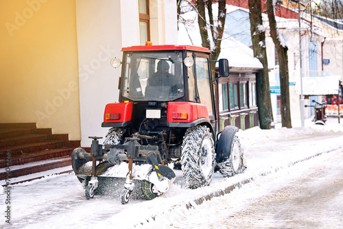 Tractor with rotating brush clean snow from sidewalk. Heavy duty vehicle with brush and snowplow removing snow from pedestrian zone on road. Tractor clearing . snowy streets with snow plow and brush