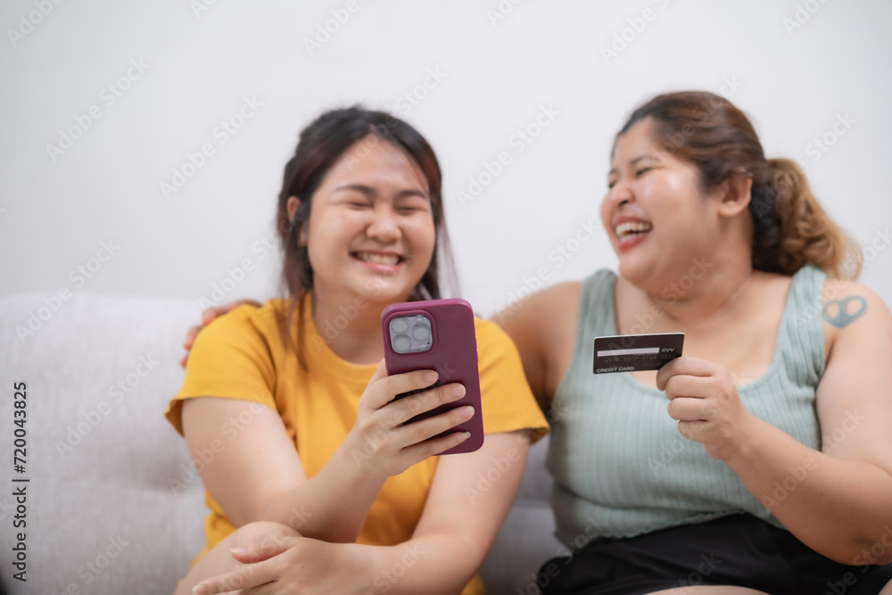 Focus at smartphone and credit card, Two Asian over weight women do online shoping at home with smile og happiness, appreciate emotion. Cozy life style at home. Focus at smartphone and credit card, Two Asian over weight women do online shoping at home with smile og happiness, appreciate emotion. Cozy life style at home.