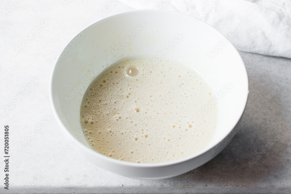 Eggs and sugar that has been whisked together in a white mixing bowl till pale and fluffy, Egg and sugar in a white bowl, process of making cake Eggs and sugar that has been whisked together in a white mixing bowl till pale and fluffy, Egg and sugar in a white bowl, process of making cake