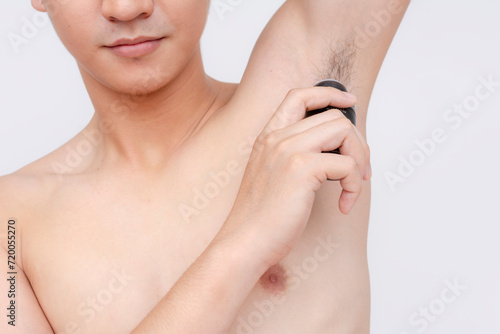 An anonymous man applies roll-on deodorant to his underarms after a bath. Body hygiene and odor prevention. Isolated on a white backdrop.