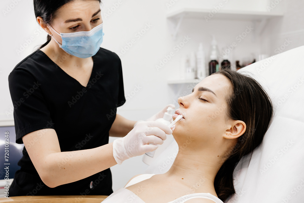 Cosmetology clinic, the doctor applies anesthesia to the patient's lips, anesthetic before injecting hyaluronic acid. Anesthetic ointment is applied before the injection procedure.