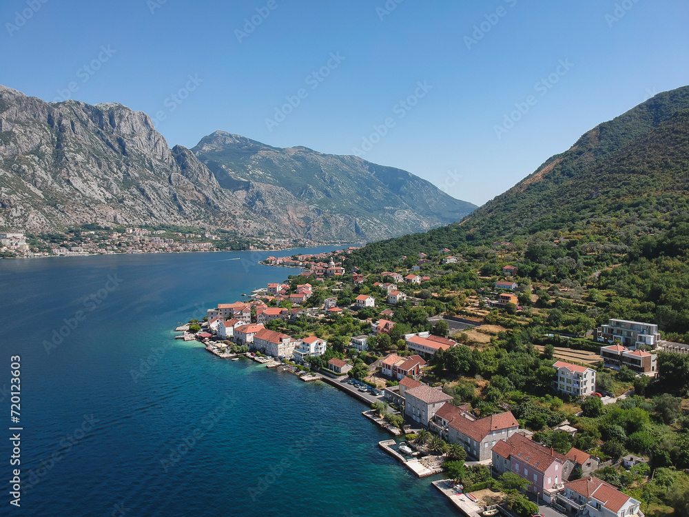 Bird's eye view of a charming village of Prcanj along the azure waters of Kotor Bay, encircled by the lush mountains of Montenegro.