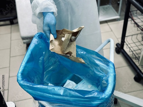 Hospital worker discarding infectious medical waste into disposal container bin. Close up of biohazard contaminated clinical waste