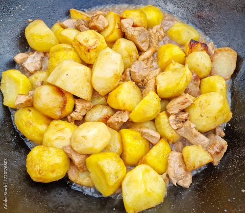 Close-up - potatoes cut into pieces are fried with meat in a cast iron cauldron