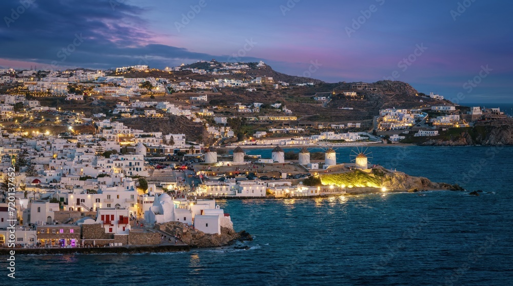 Aerial view of the illuminated old town of Mykonos island until the famous windmills during evening, Cyclades, Greece