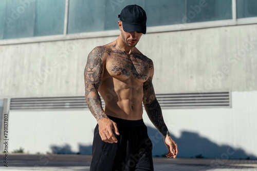 Chico joven tatuado y musculoso posando sin camiseta en la calle con ropa urbana