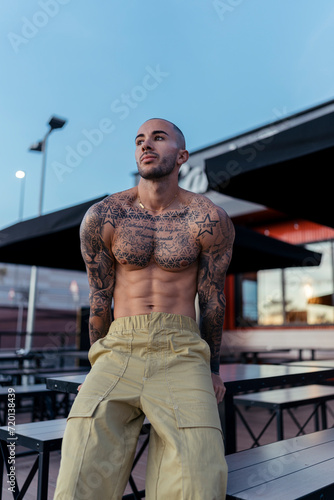 Chico tatuado y musculoso posando sin camiseta en terraza de restaurante de comida rapida