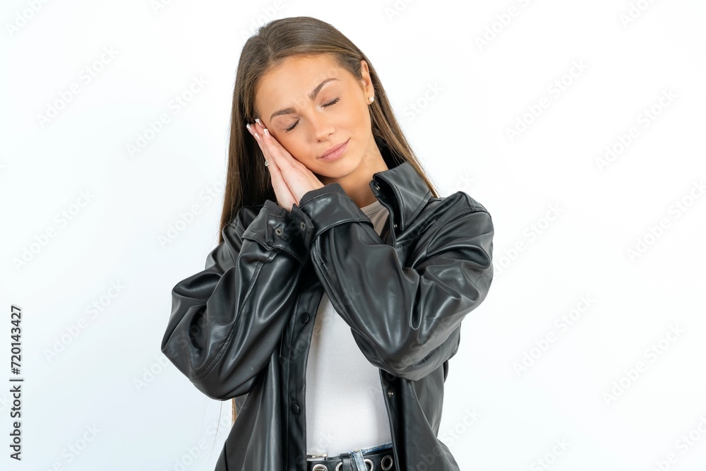 beautiful girl wearing biker jacket sleeping tired dreaming and posing with hands together while smiling with closed eyes.