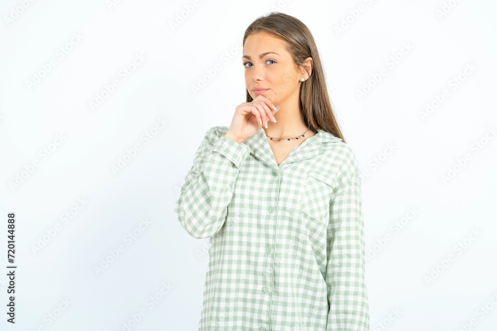 Beautiful young woman wearing green plaid pyjama looking confident at the camera smiling with crossed arms and hand raised on chin. Thinking positive. Beautiful young woman wearing green plaid pyjama looking confident at the camera smiling with crossed arms and hand raised on chin. Thinking positive.