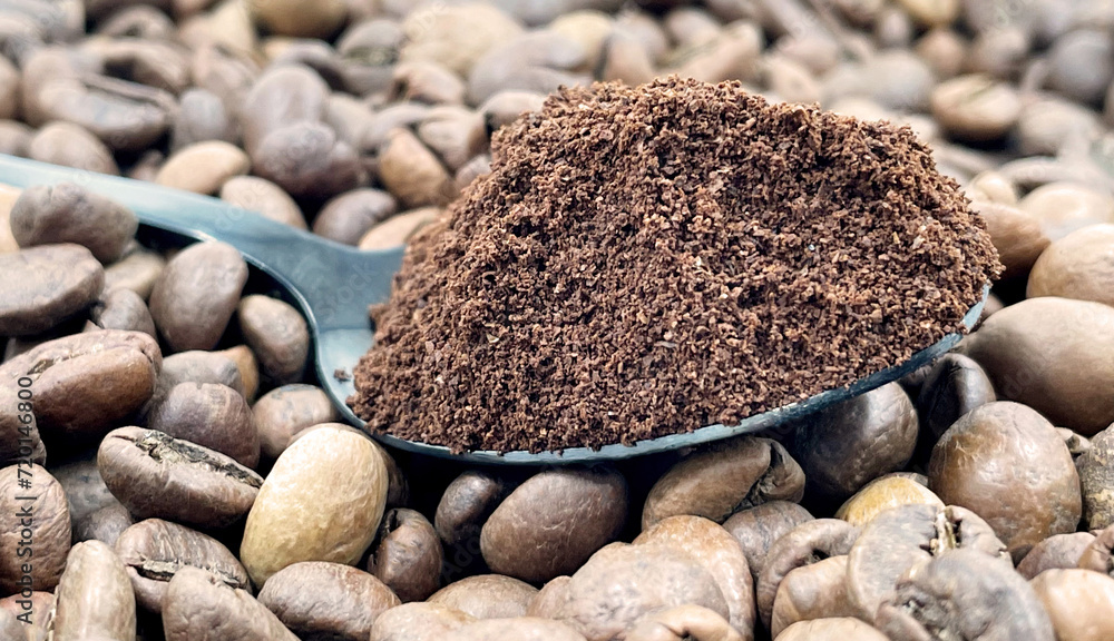 Against the background of roasted aromatic coffee beans lies a metal spoon filled with ground coffee. A drink made from roasted and ground beans from the coffee tree or coffee bush. Against the background of roasted aromatic coffee beans lies a metal spoon filled with ground coffee. A drink made from roasted and ground beans from the coffee tree or coffee bush.