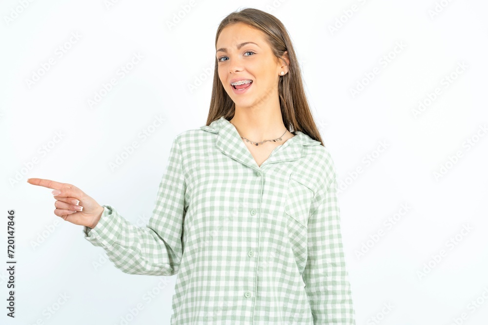 Beautiful young woman wearing green plaid pyjama laughs happily points away on blank space demonstrates shopping discount offer, excited by good news or unexpected sale. Beautiful young woman wearing green plaid pyjama laughs happily points away on blank space demonstrates shopping discount offer, excited by good news or unexpected sale.