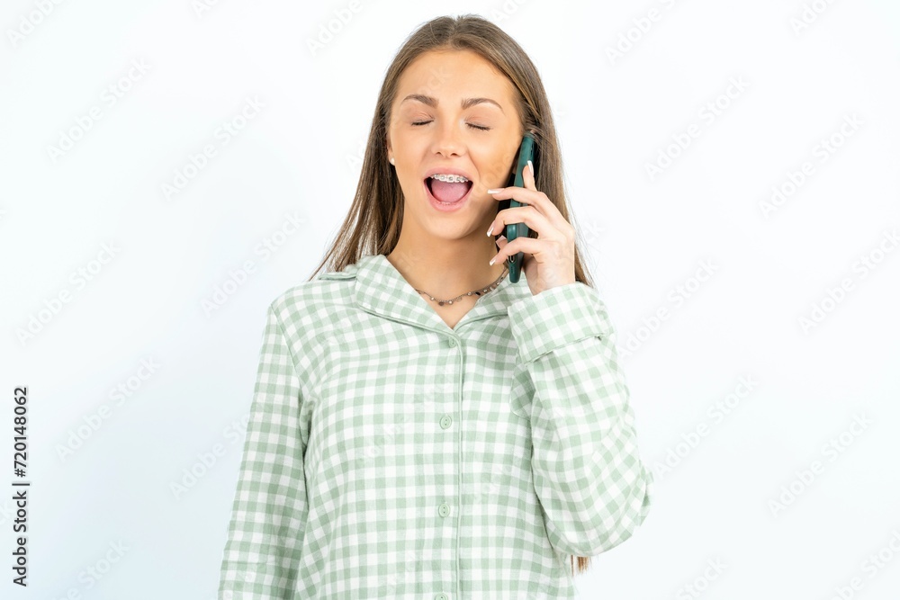 Overemotive happy Beautiful young woman wearing green plaid pyjama laughs out positively hears funny story from friend during telephone conversation Overemotive happy Beautiful young woman wearing green plaid pyjama laughs out positively hears funny story from friend during telephone conversation