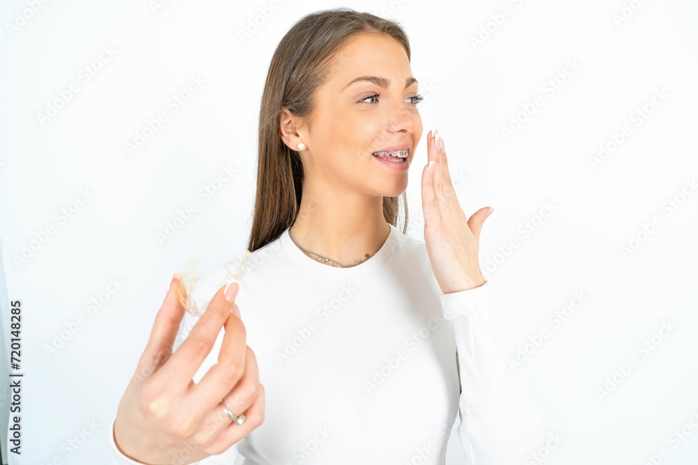 Happy young beautiful girl wearing white T-shirt holding and showing at camera an invisible aligner while laughing. Dental healthcare and confidence concept. Happy young beautiful girl wearing white T-shirt holding and showing at camera an invisible aligner while laughing. Dental healthcare and confidence concept.